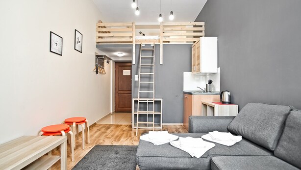 A compact living space with a bunk bed, kitchenette, grey sofa, and a small dining area. - Smart Rooms for Rent (Kraków)
