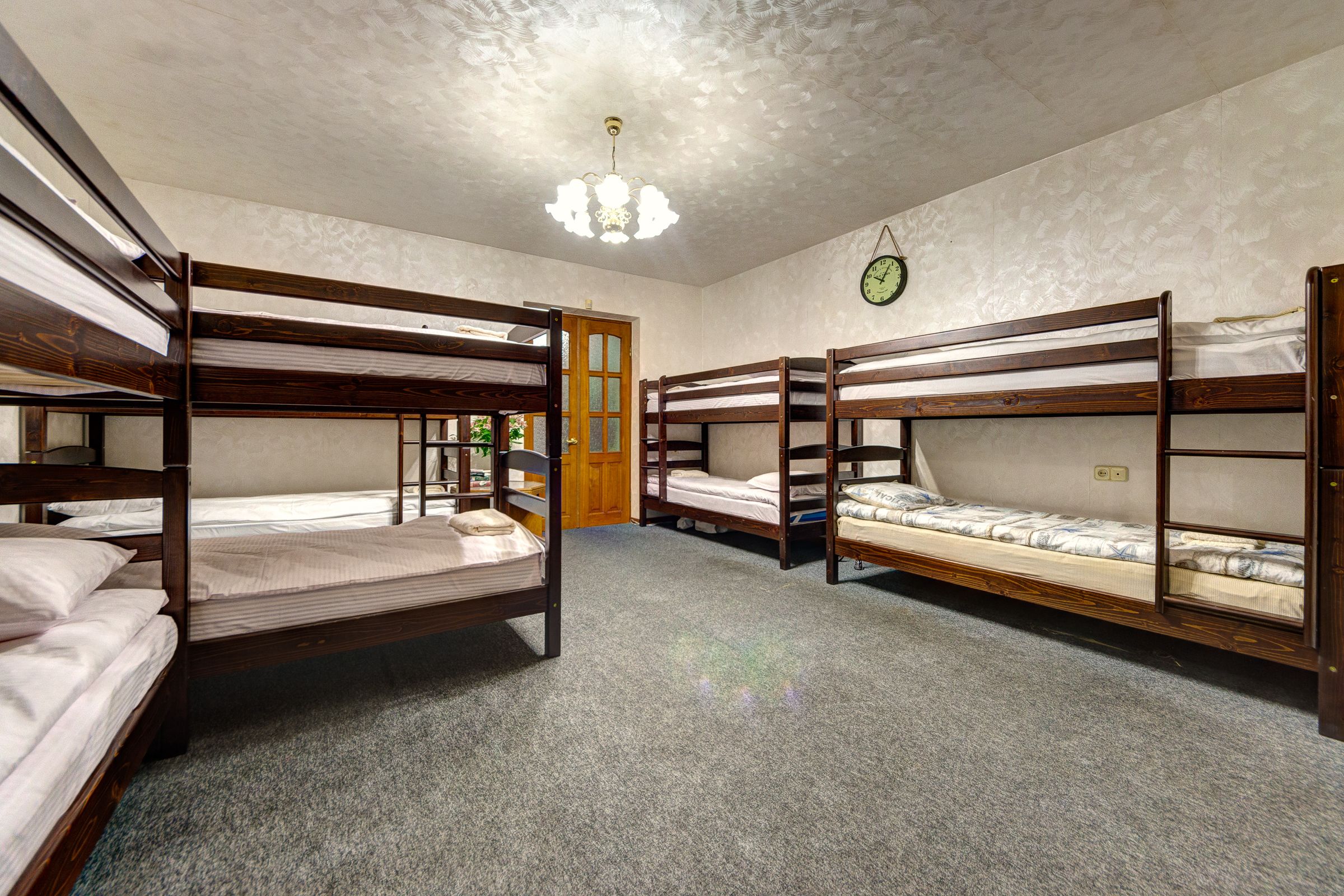A room with bunk beds, a wooden door, a clock on the wall, and a chandelier.