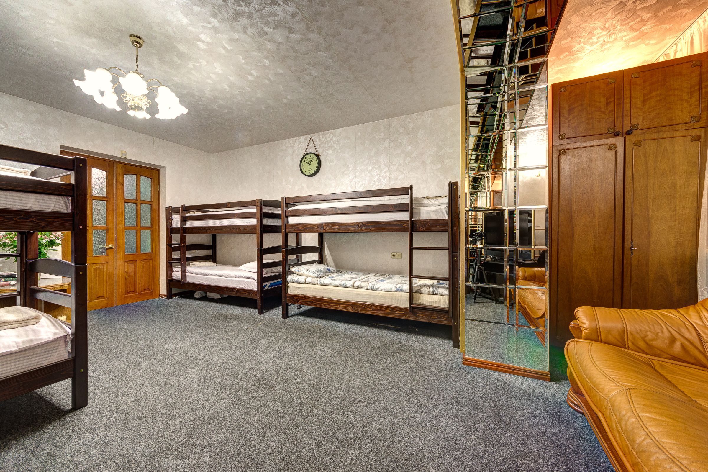 A room with bunk beds, a wooden wardrobe, a leather sofa, and a chandelier.