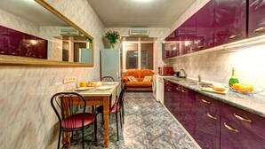 A compact kitchen with a dining area, marble flooring, and purple cabinets. - Dikat Hostel (Kyiv)
