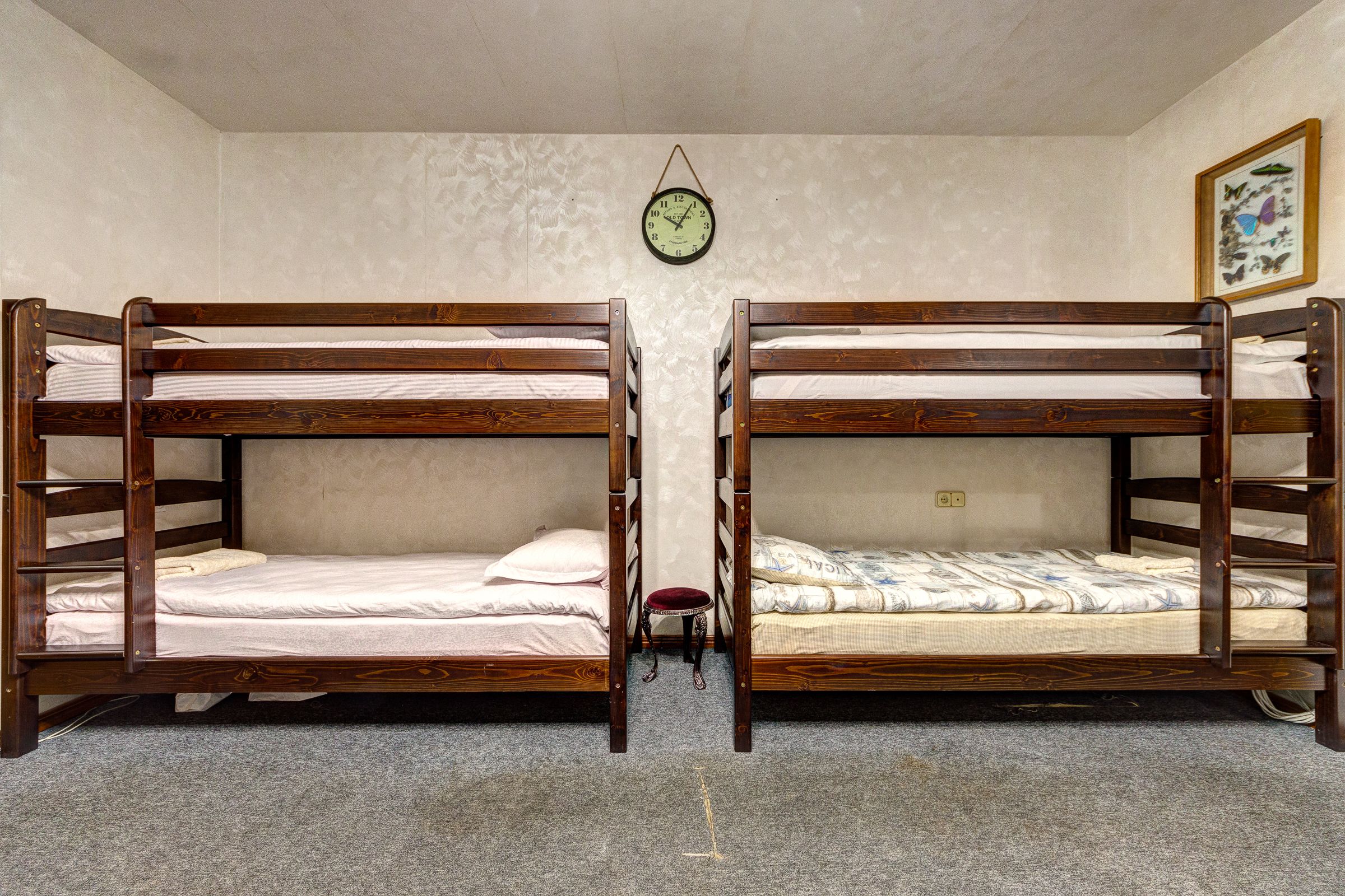 Una habitación con dos literas, un taburete pequeño, un reloj y un cuadro en la pared.