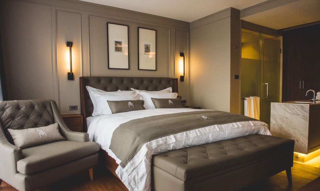 Une chambre avec un grand lit, une chaise, un banc et une salle de bain visible.