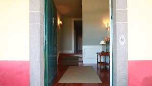 A hallway with a green door, a wooden bench, a lamp, and a vase with flowers. - Quinta das Malvas (Funchal)