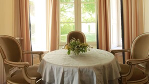 A dining table with a floral centerpiece, surrounded by two chairs, in a room with large windows and curtains. - Quinta das Malvas (Funchal)