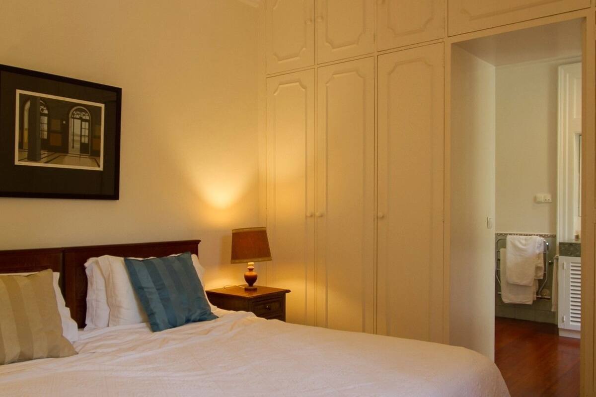 A hotel room with a large bed, two bedside tables with lamps, a framed picture on the wall, and a wardrobe.