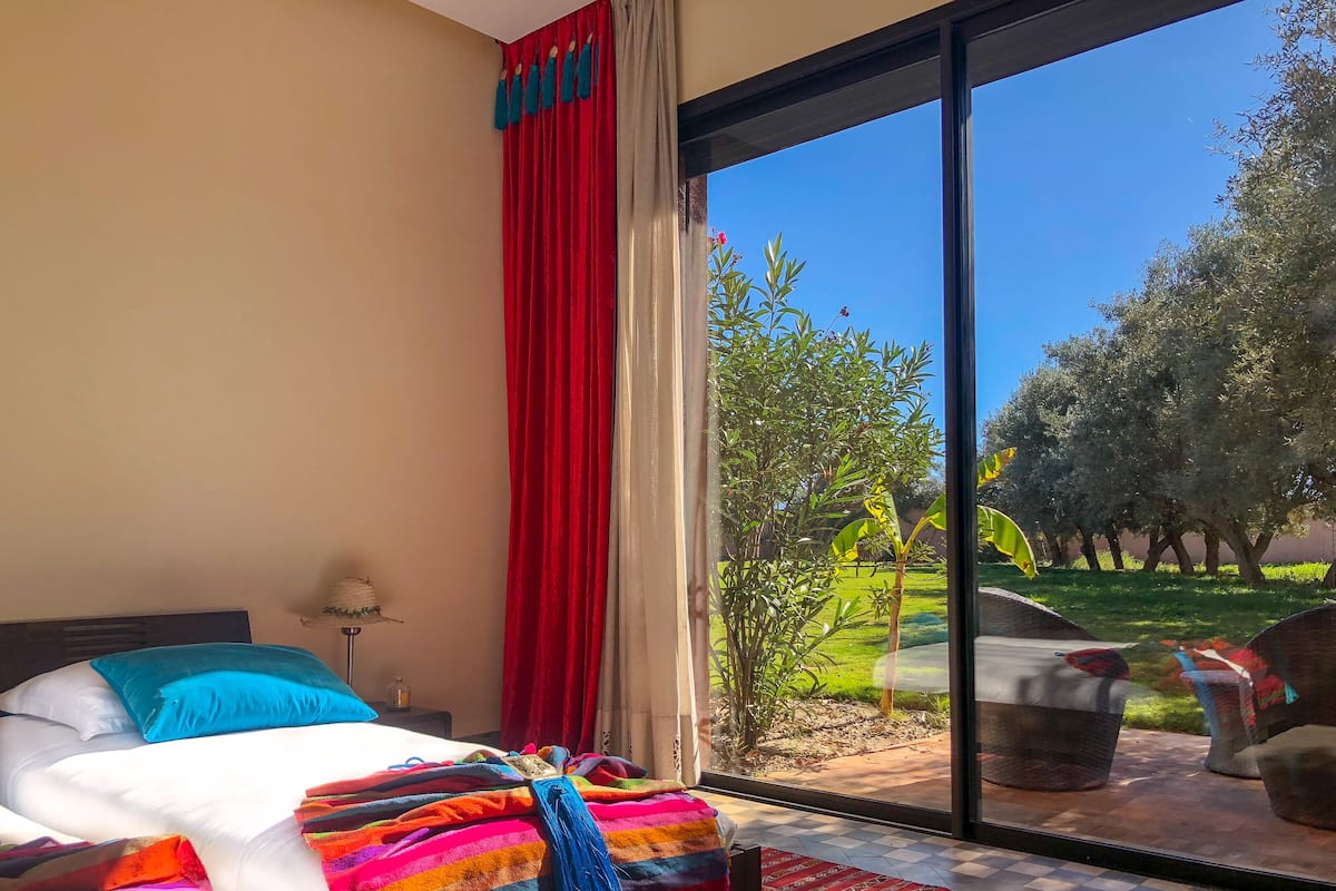A bedroom with a large bed, a view of the outdoors through a sliding glass door, and a red curtain.