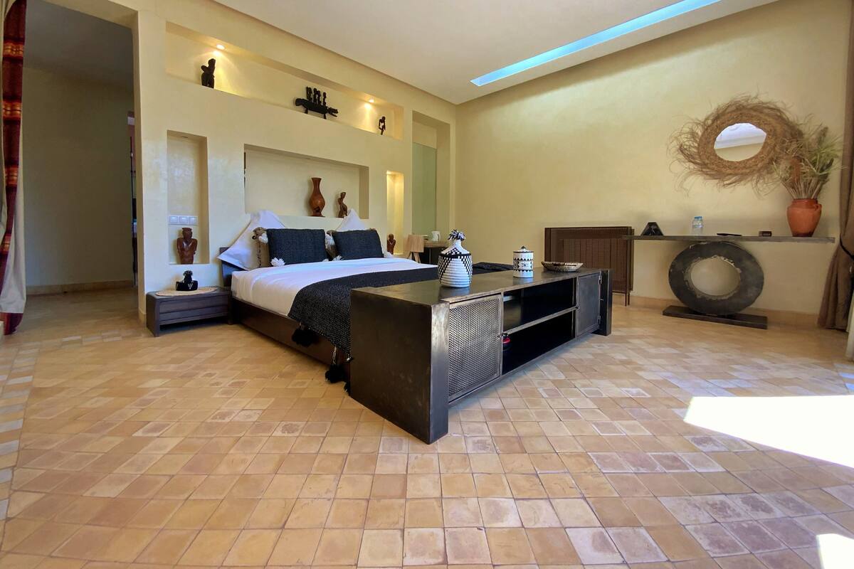 A modern bedroom with a large bed, a console table, and a wall-mounted shelf with decorative items.