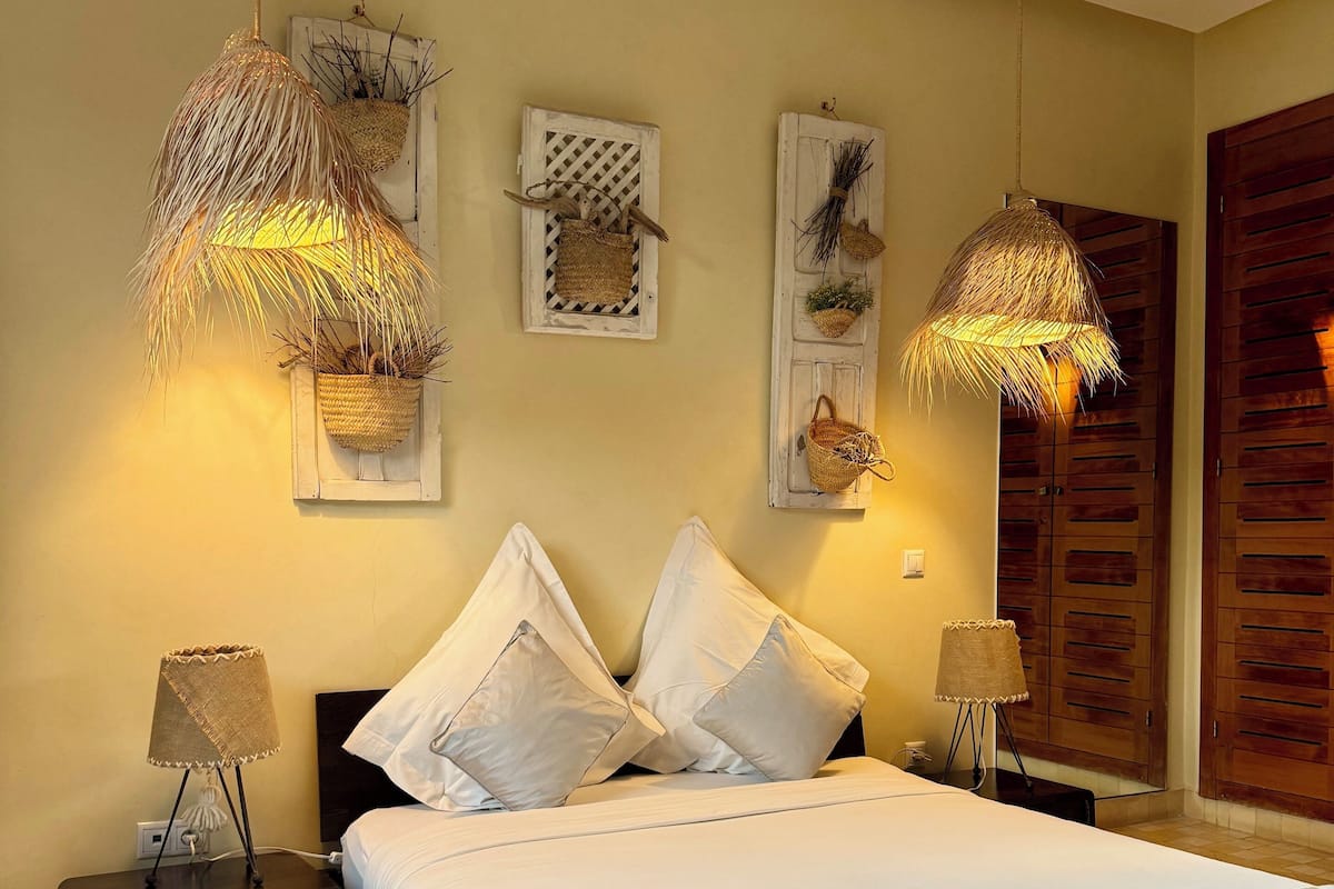 A neatly arranged bedroom with a large bed, two bedside tables with lamps, a patterned rug, and wall-mounted decorations.