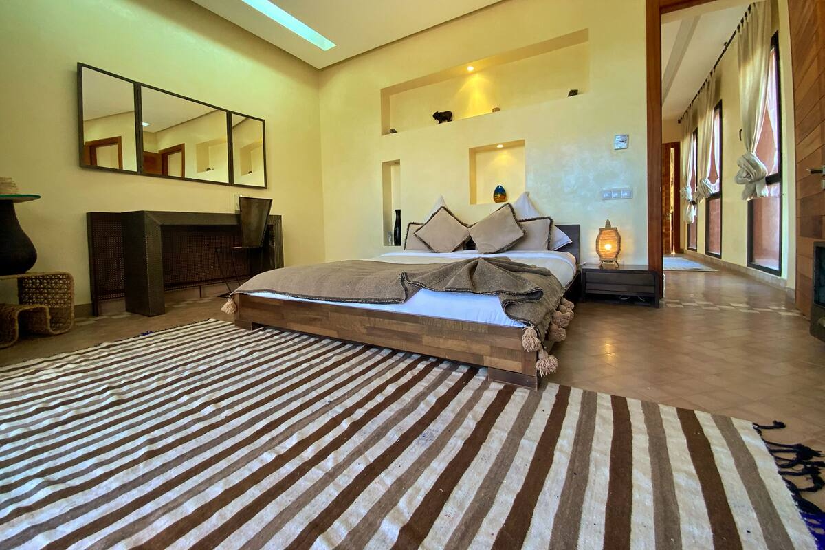 A spacious bedroom with a large bed, a mirror, a fireplace, and a view of a corridor.