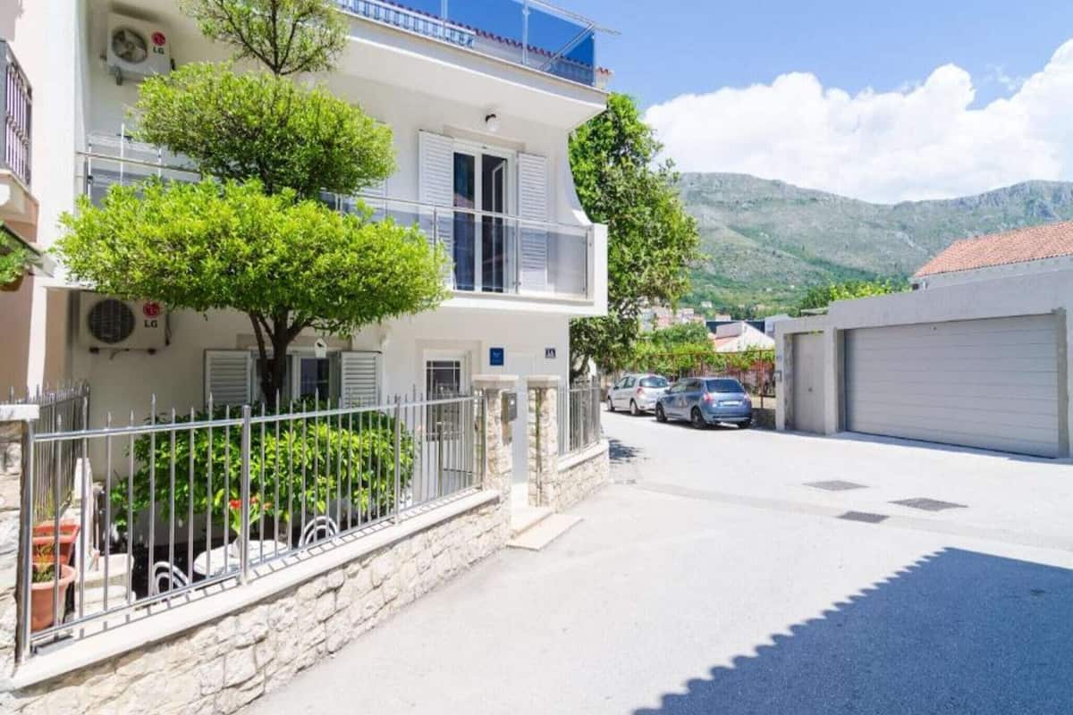 Un bâtiment à deux étages doté d’un balcon, d’un mur en pierre et d’une voiture garée dans l’allée.