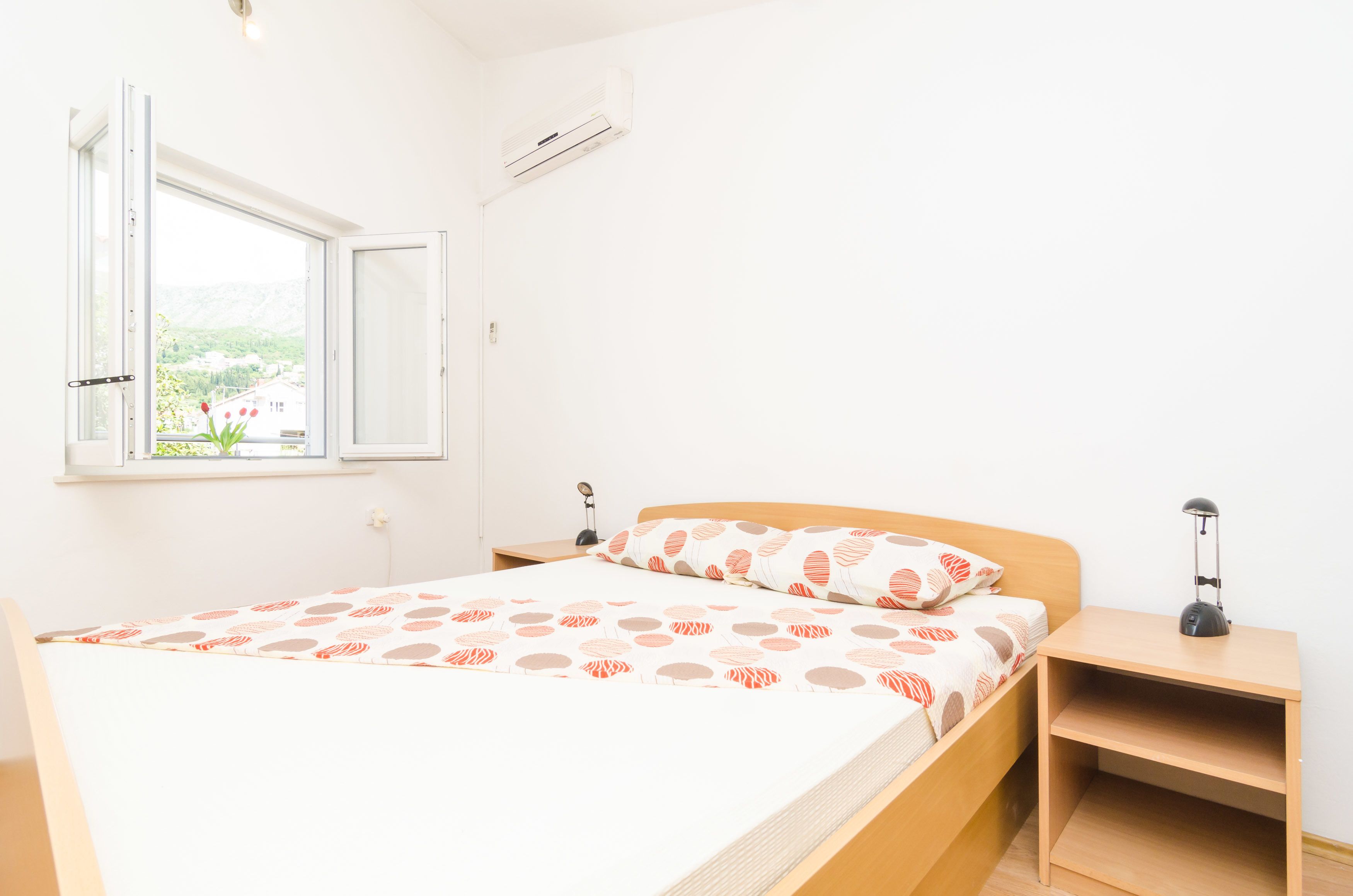 Un dormitorio ordenado con cama, mesitas de noche y ventana con vistas abiertas.