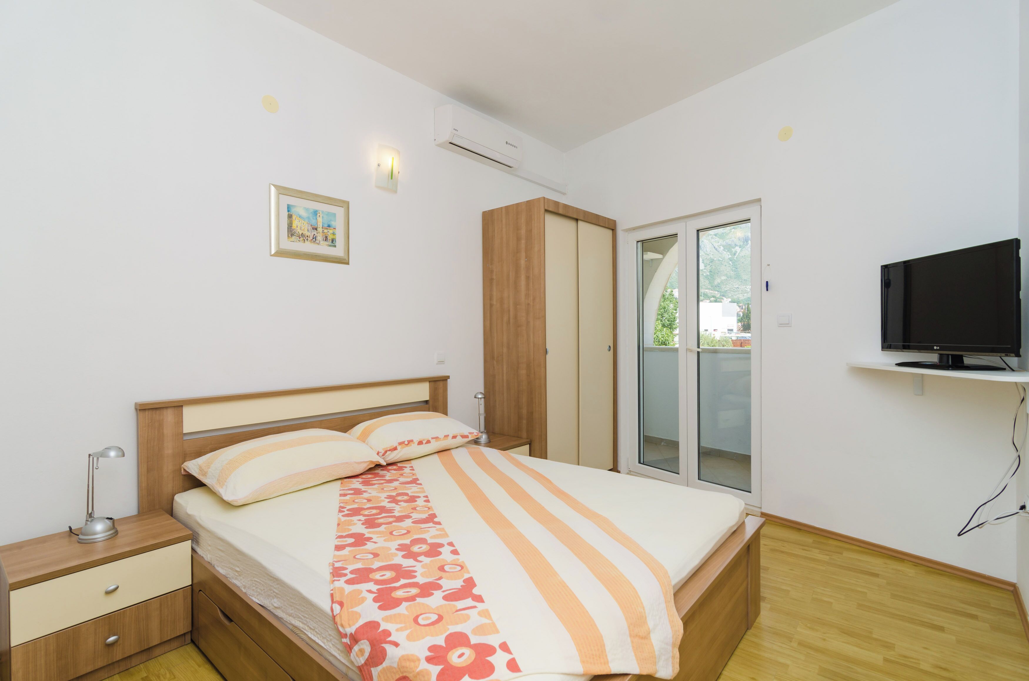 Quarto com cama, mesa de cabeceira, guarda-roupa, televisão e porta de vidro deslizante para o exterior.