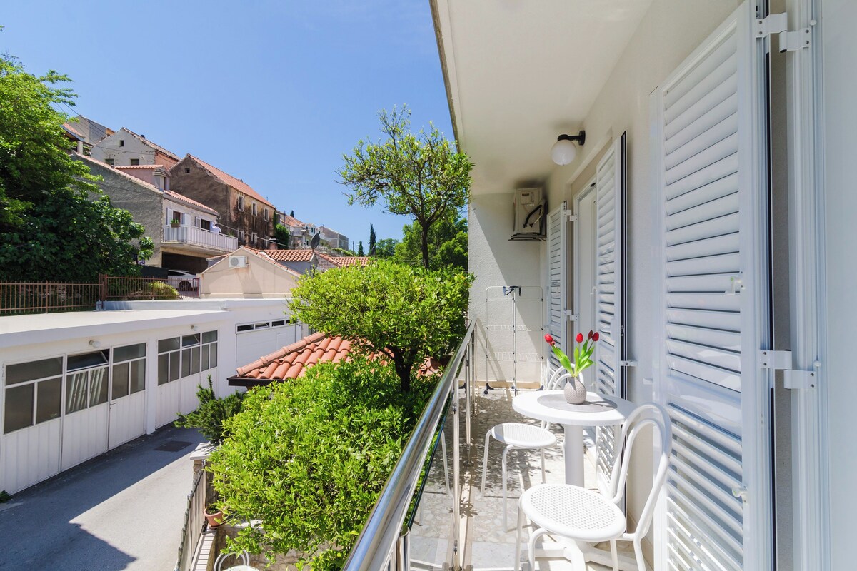 A balcony with a white table and chairs, a potted plant, and a view of the street below.