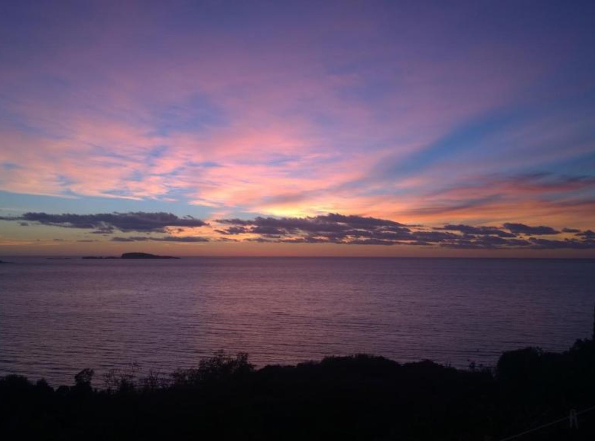 Un atardecer sobre un mar tranquilo con una isla distante.