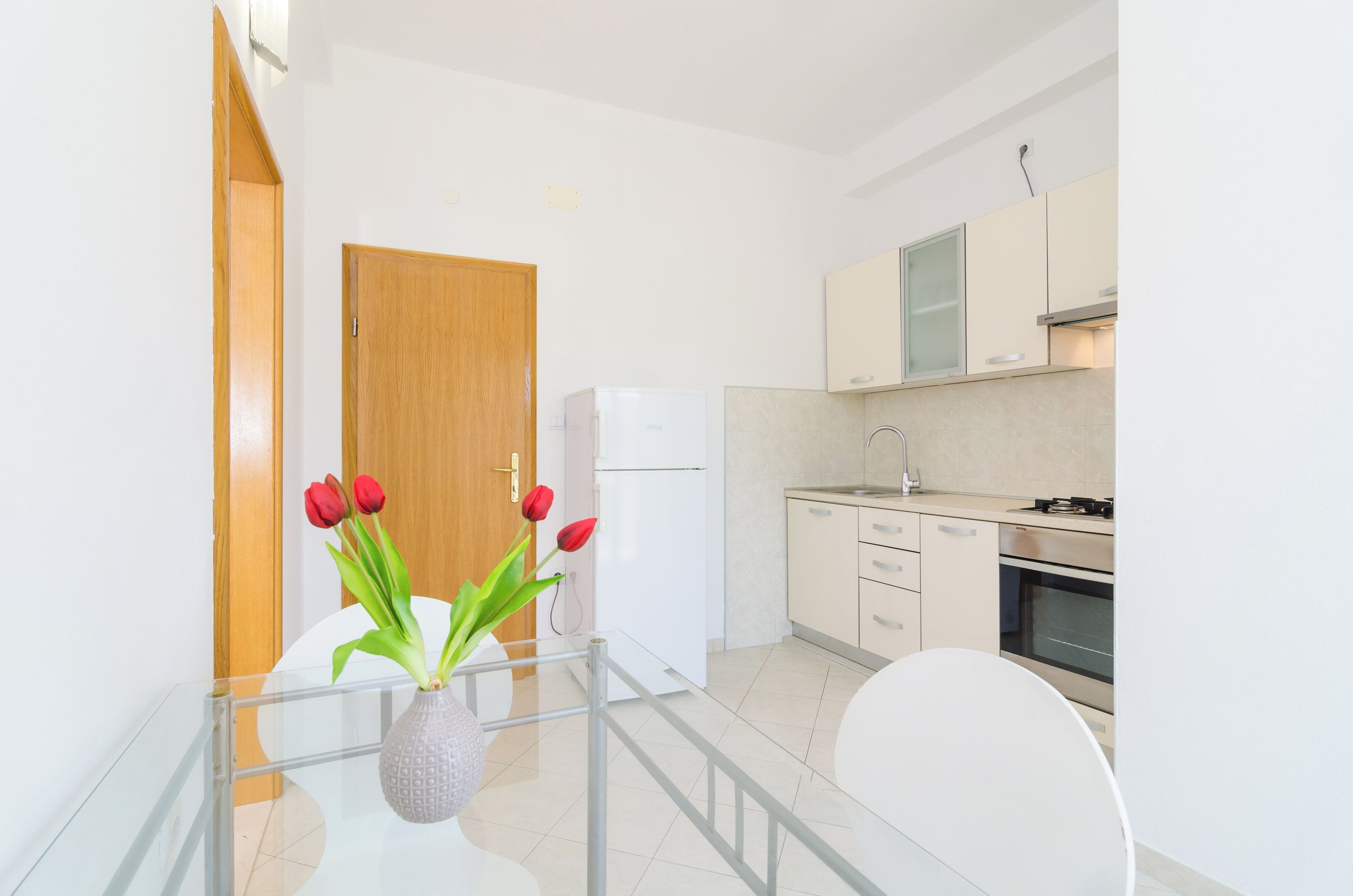 Une cuisine moderne avec des meubles blancs, un four en acier inoxydable et une table en verre sur laquelle est posé un vase de tulipes rouges.