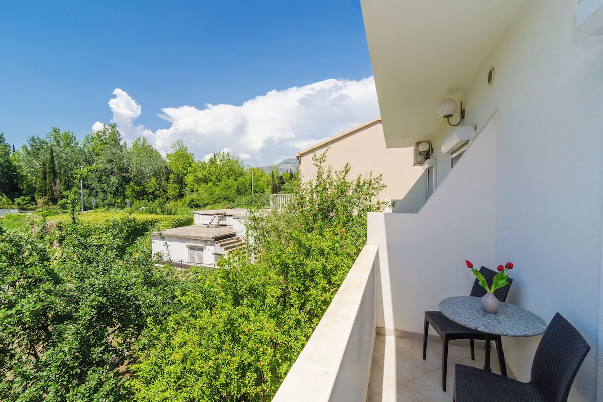 Un balcon avec une table et des chaises, donnant sur un jardin et des immeubles.