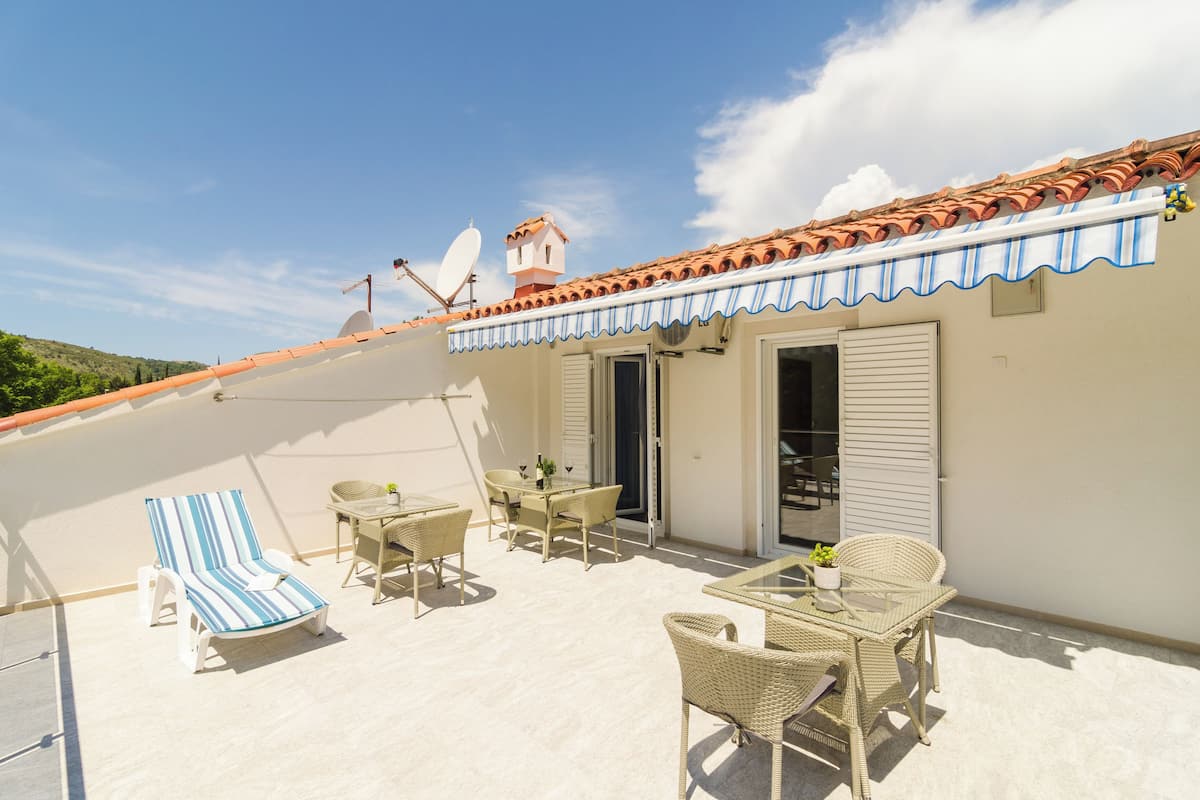 Une terrasse sur le toit, dotée d’un toit en tuiles, d’une antenne parabolique et d’un espace abrité avec des meubles en osier et un fauteuil de jardin à rayures.