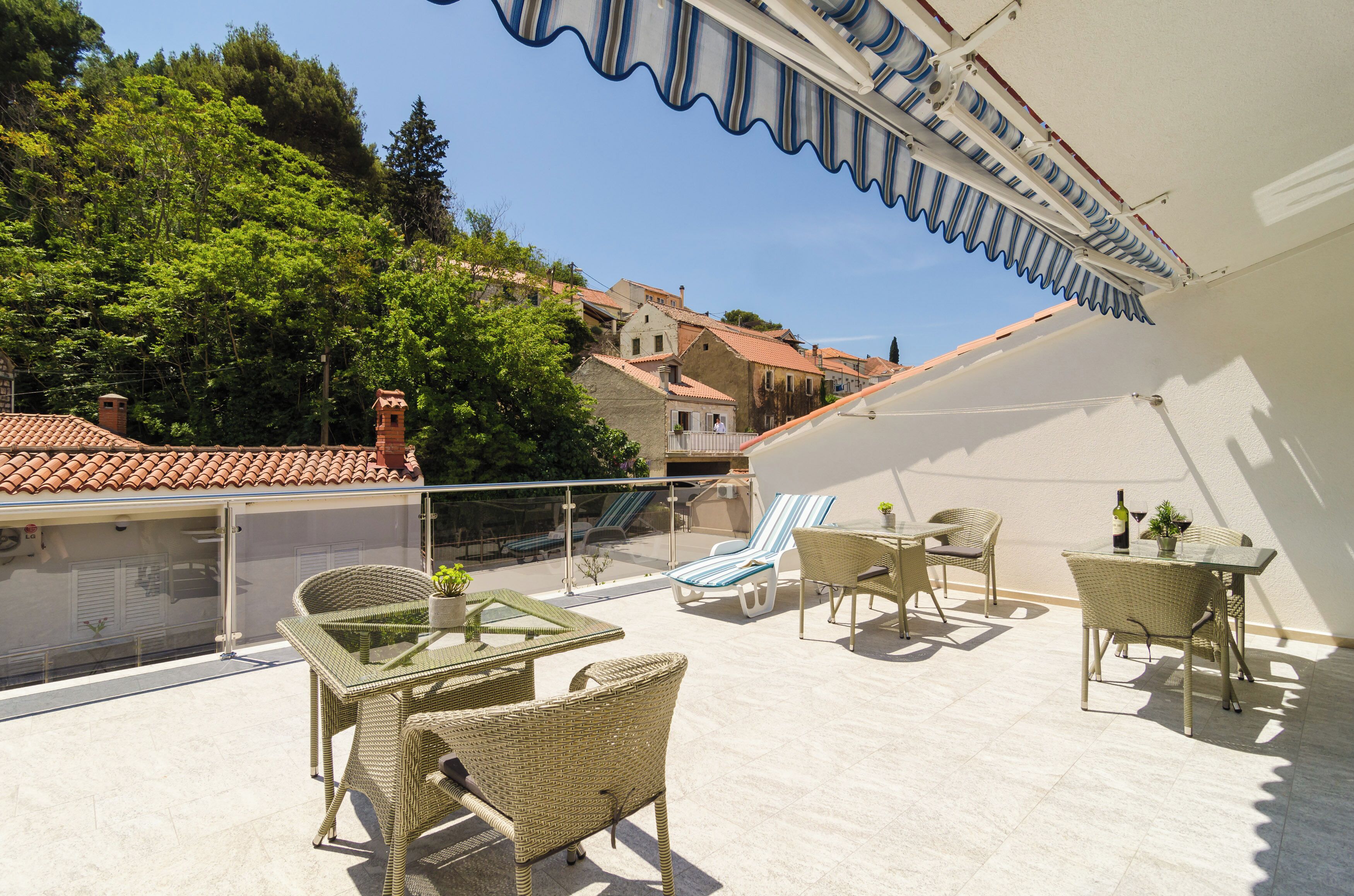 Eine Dachterrasse mit Korbmöbeln, einem Glastisch und Blick auf die umliegenden Gebäude und Bäume.