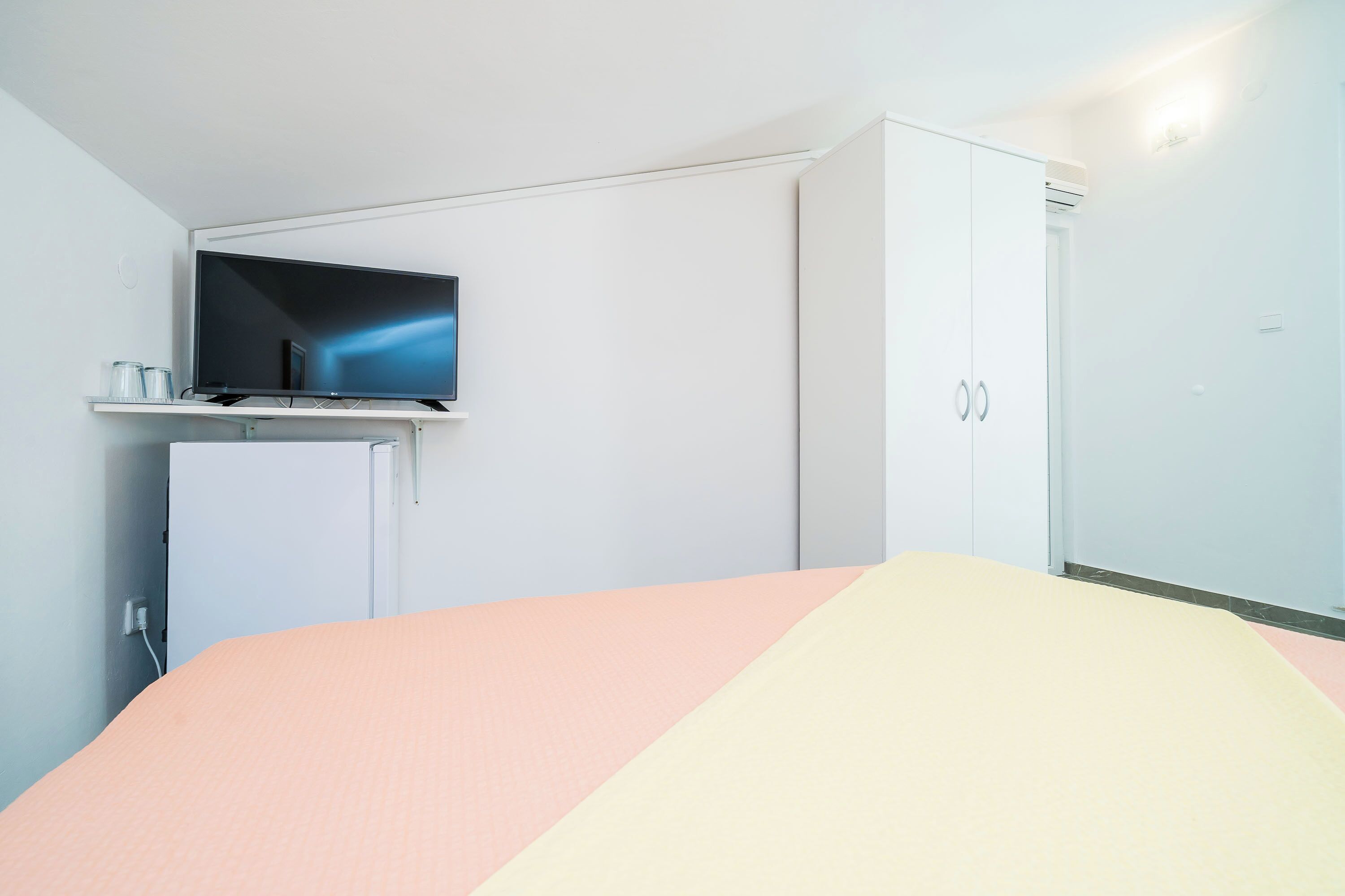 Een slaapkamer met een bed, een televisie op een standaard, een kledingkast en een deur.
