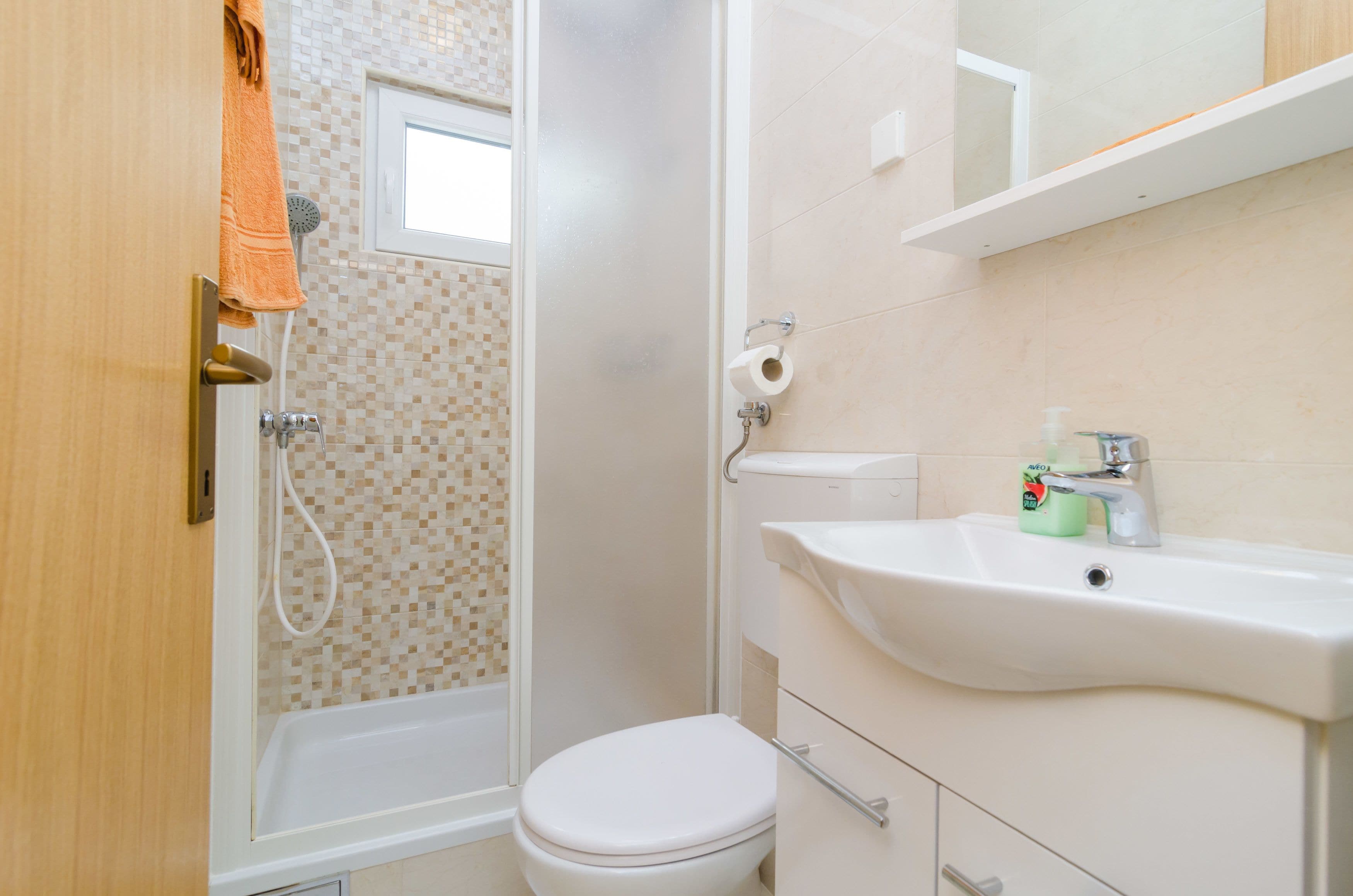 A bathroom with a shower, toilet, sink, and a small window.