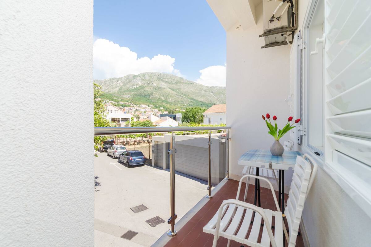 Un balcon donnant sur la ville et les montagnes, une table avec des chaises et un vase rempli de fleurs.