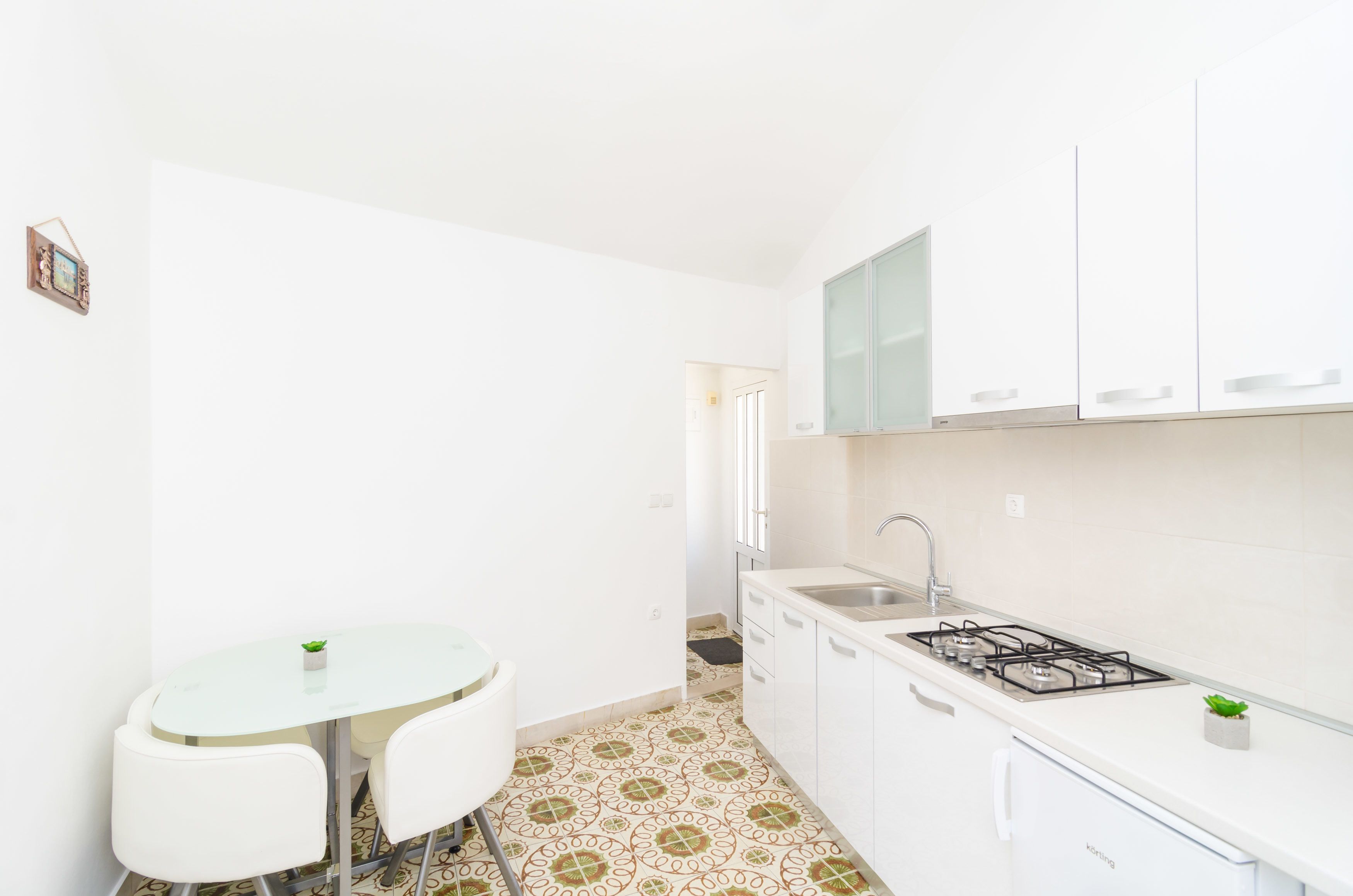 Cocina compacta con armarios blancos, estufa a gas, lavamanos y una pequeña mesa de comedor con sillas.