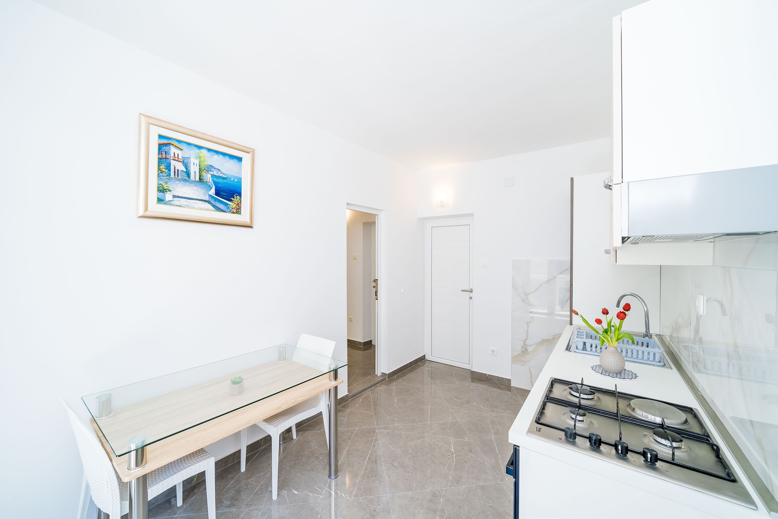 A modern kitchen with a gas stove, a dining table with chairs, and a framed painting on the wall.