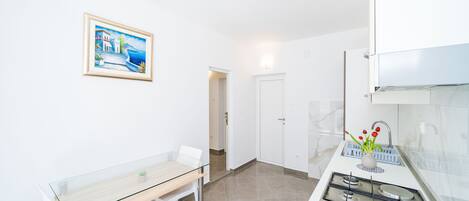 A modern kitchen with a gas stove, a dining table with chairs, and a framed painting on the wall.