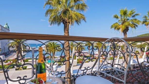 En balkong med utsikt över havet, palmer och en flaska champagne.
