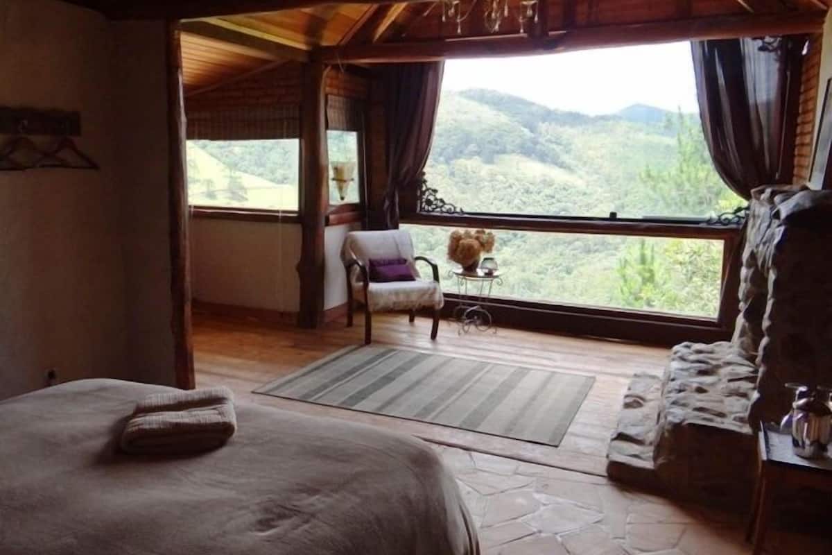 Une pièce comprenant un lit, une chaise, une petite table avec un vase et donnant sur l’extérieur.