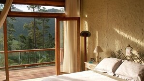 Een slaapkamer met een groot raam, een bed, een nachtkastje en een lamp.