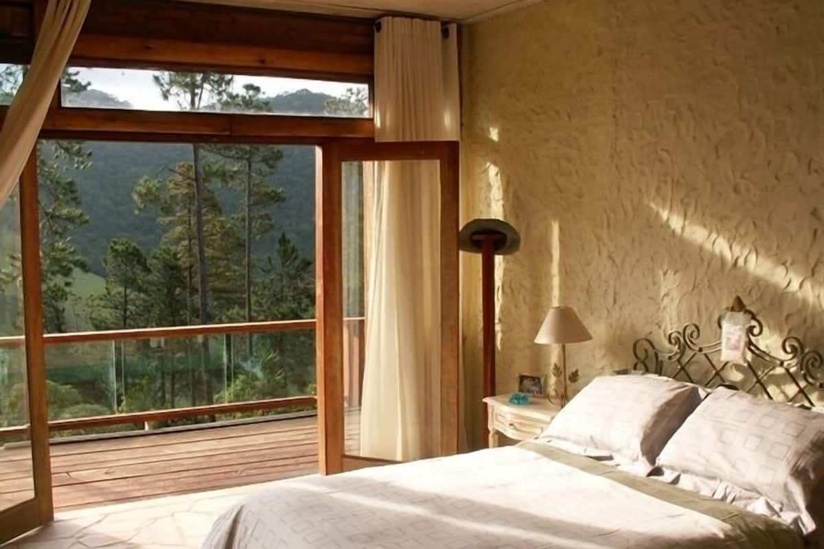 Une chambre avec une grande fenêtre, un lit, une table de chevet et une lampe.