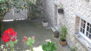 A courtyard with a stone wall, potted plants, and a window. - Le Havre de Bennecourt (Bennecourt)