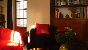 A cozy living room with a red sofa, a black armchair with a red cushion, and a bookshelf filled with books and decorative items. - Le Havre de Bennecourt (Bennecourt)