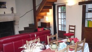A cozy dining area with a red upholstered bench, a wooden dining table set with a vase, teapot, and plates, and a staircase leading to a second floor. - Le Havre de Bennecourt (Bennecourt)