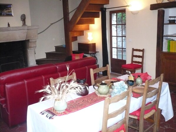 A cozy dining area with a red upholstered bench, a wooden dining table set with a vase, teapot, and plates, and a staircase leading to a second floor.