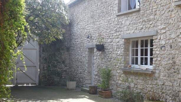 A stone building with a large garage door, a window with a white frame, and several potted plants. - Le Havre de Bennecourt (Bennecourt)