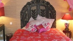 A bed with a red floral bedspread, a decorative headboard, and pink curtains with tassels. - Le Havre de Bennecourt (Bennecourt)