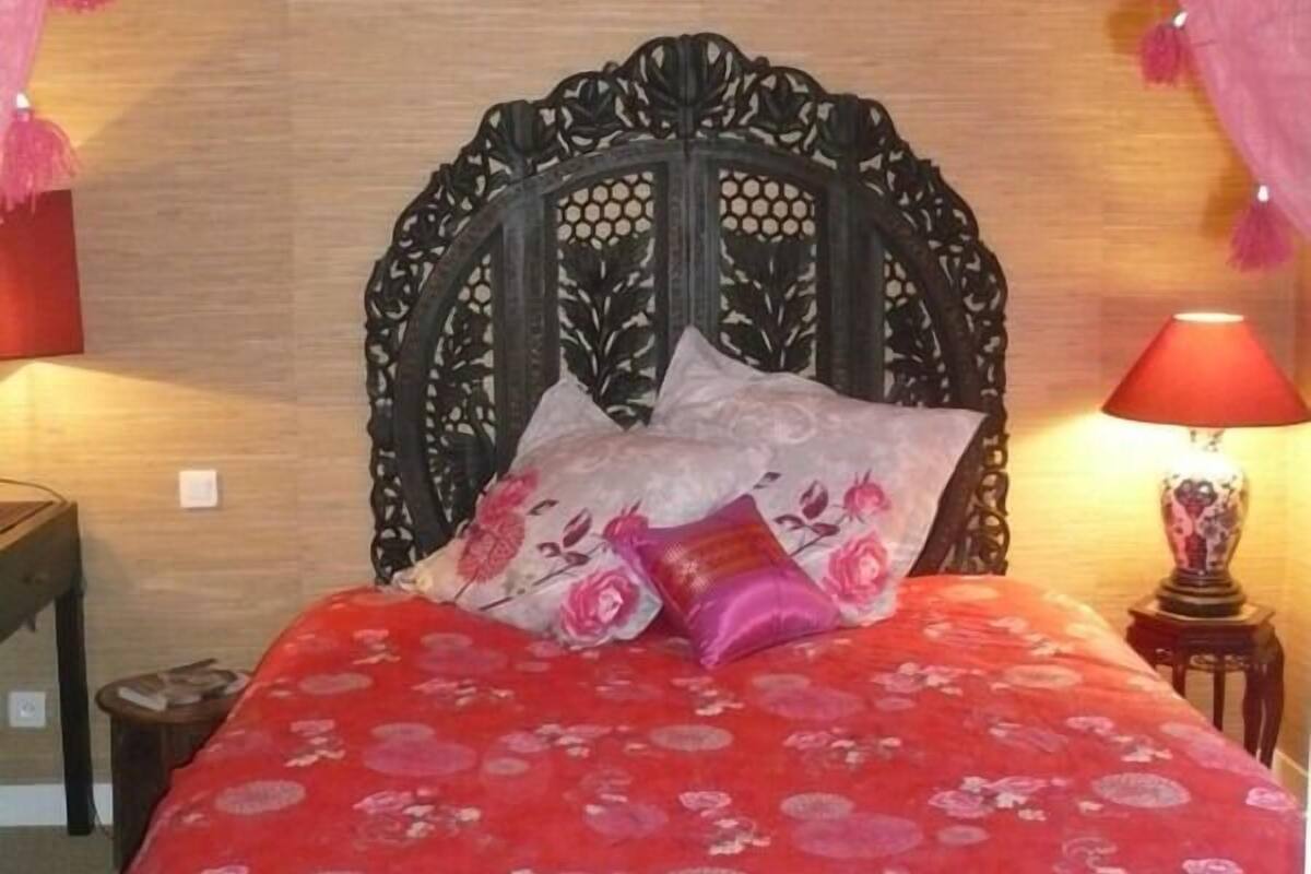 A bed with a red floral bedspread, a decorative headboard, and pink curtains with tassels.