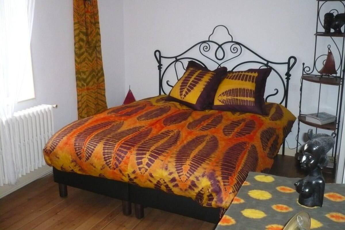 A bed with a patterned bedspread, a black metal headboard, and a small shelf with decorative items.