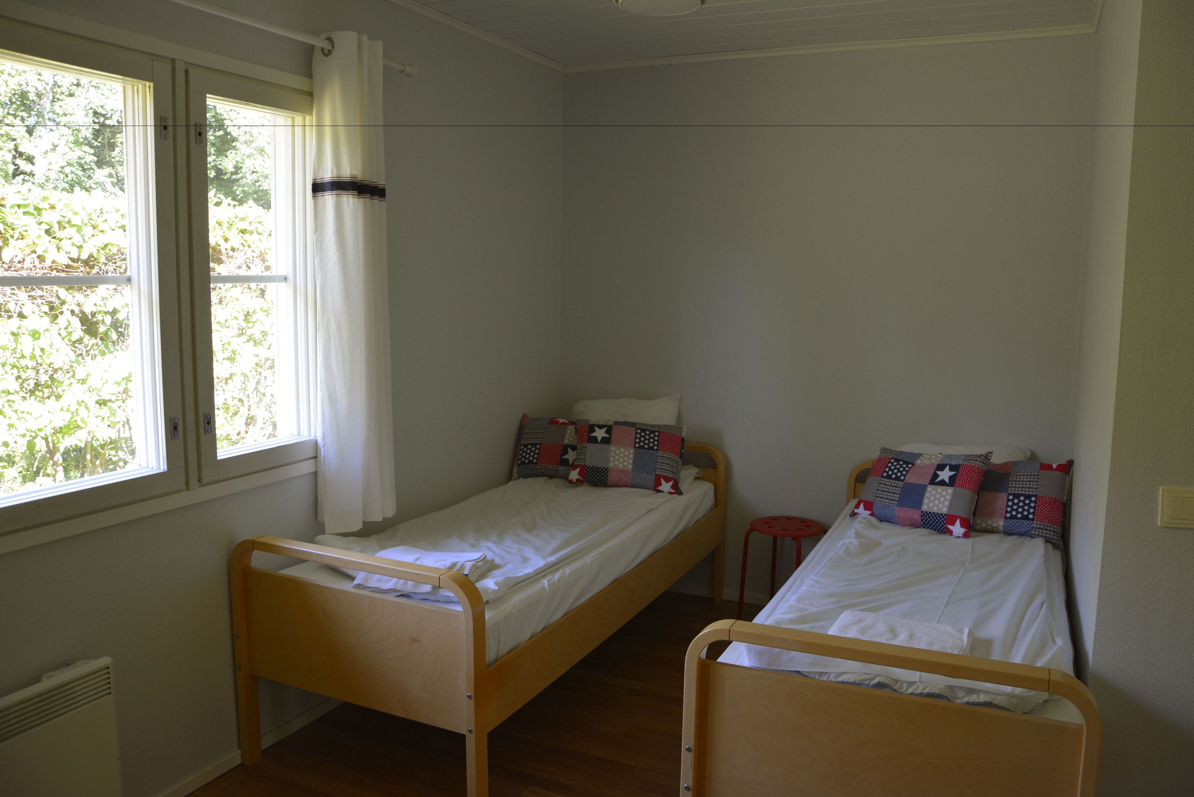 A room with two single beds, a window with curtains, and a radiator.