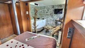 A bedroom with a bed, wooden walls, a stone wall, a bathtub, and a wooden bench. - VIP Paris Yacht Hotel (Paris)