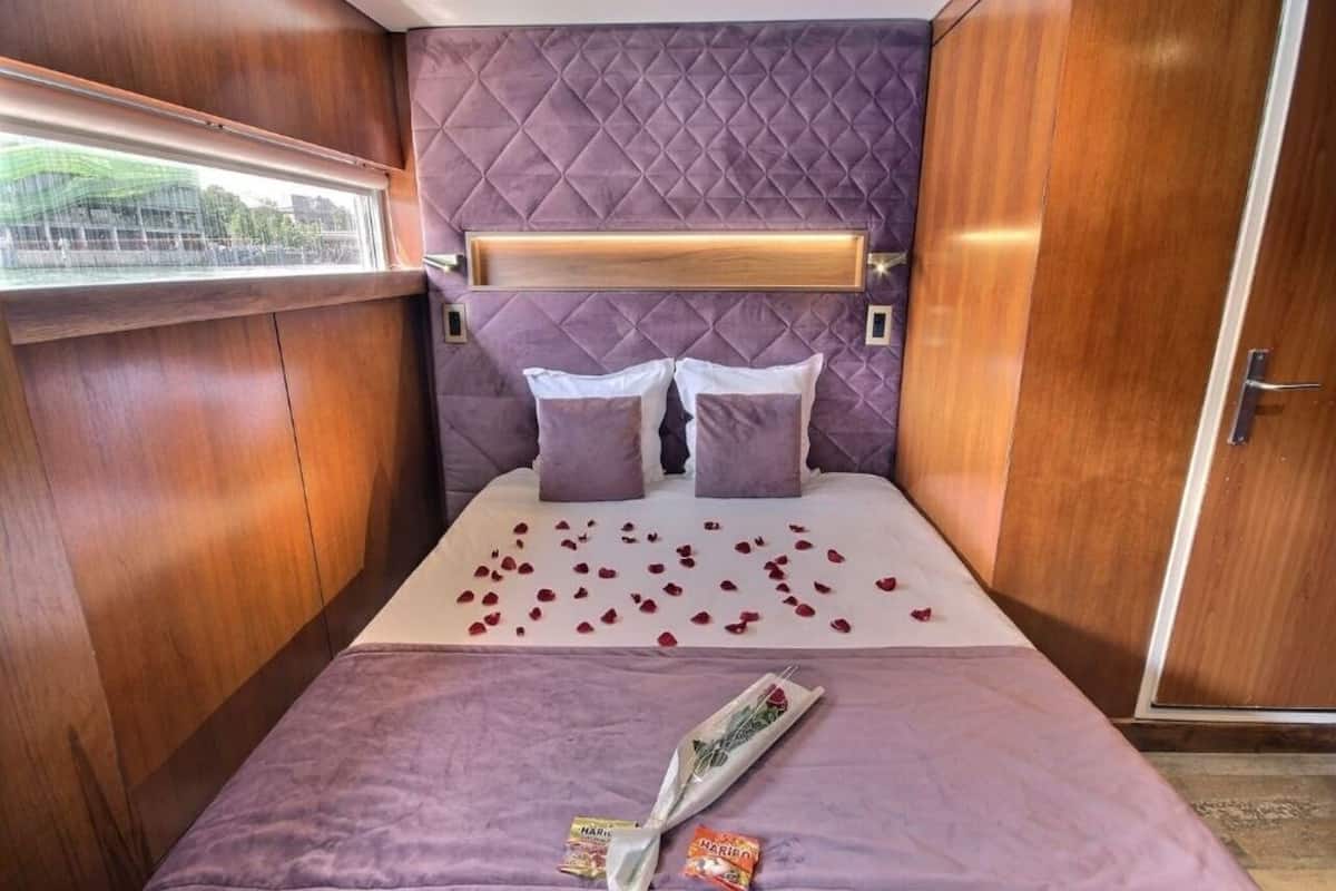 Ein Bett mit violettem Kopfteil, zwei Kissen und Rosenblätter, die auf dem Bett verteilt sind.