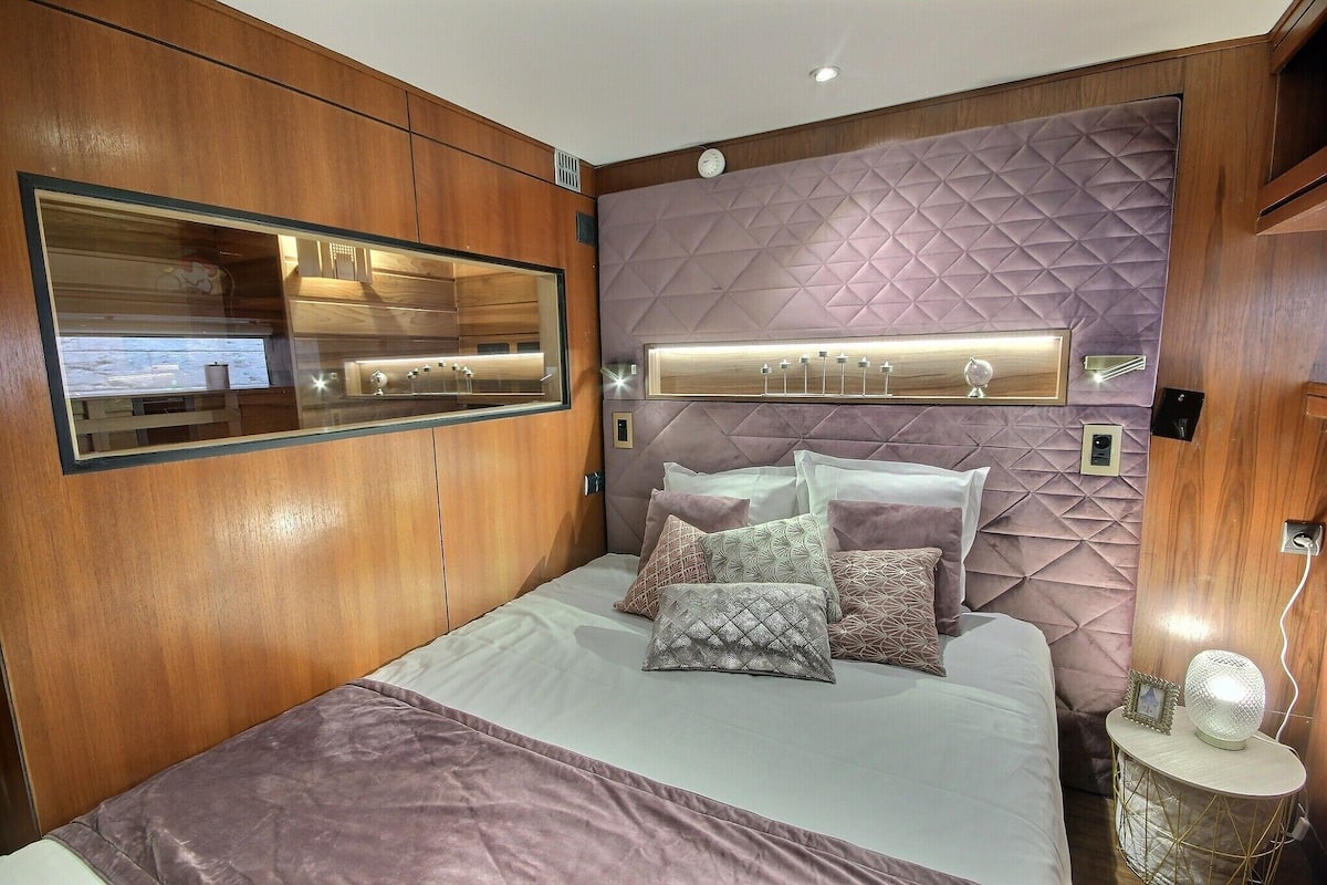 Ein modernes Schlafzimmer mit einem großen Bett, einem Spiegel, einer Schminkkommode mit Beleuchtung und einer Wanduhr.