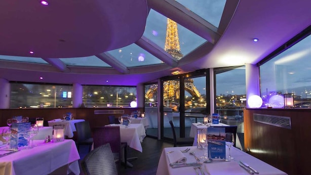 A restaurant with tables set for dining, large windows, and the Eiffel Tower in the background. - VIP Paris Yacht Hotel (Paris)