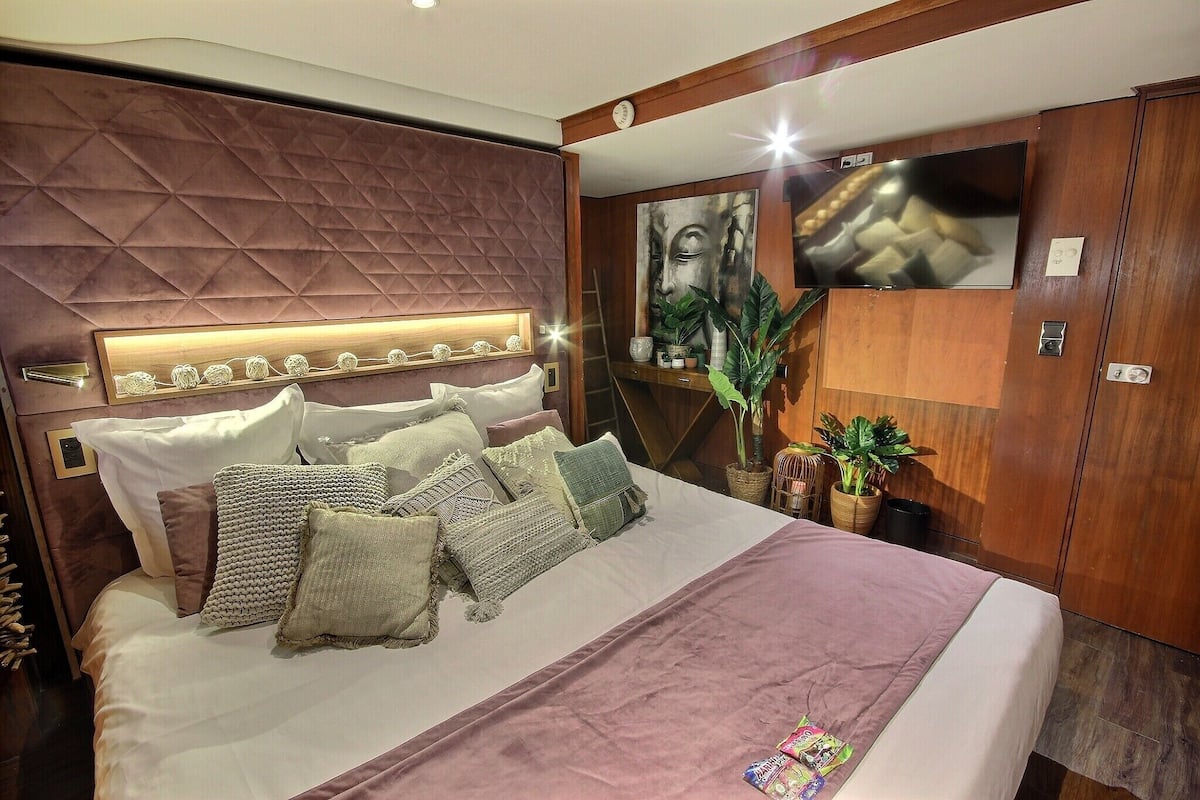 Ein modernes Schlafzimmer mit einem großen Bett, einer Kopfteil mit geometrischem Muster, einem flachbildfernseher an der Wand und einer Topfpflanze.