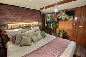 A modern bedroom with a large bed, a headboard with a geometric pattern, a flat-screen TV mounted on the wall, and a potted plant. - VIP Paris Yacht Hotel (Paris)