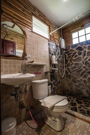 A bathroom with a stone wall, a toilet, a sink, and a shower. - Ramiarndao Boutique Place Hotel (Amnatcharoen)
