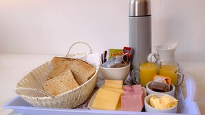 Ein Frühstücksbrett mit Brot, Käse, Schinken, Butter, Marmelade und Saft.
