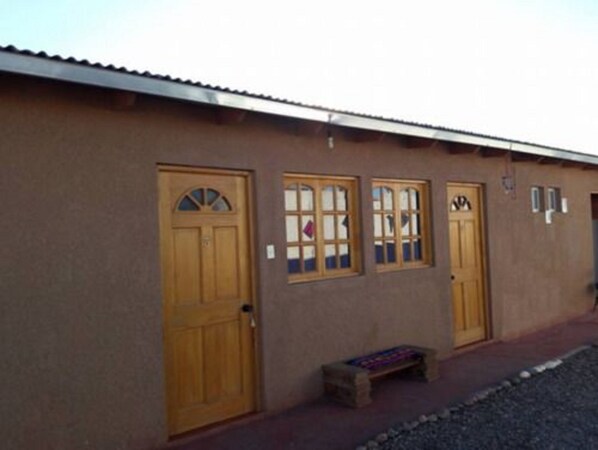 A building with three wooden doors, a small bench, and a gravel path.
